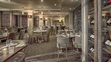 Een modern restaurant met meerdere eettafels en stoelen, een kamerbreed tapijt met patroon en een wijnrek.