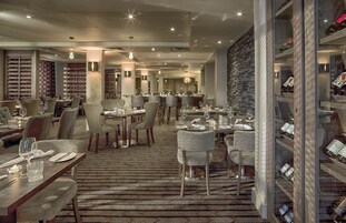 Een modern restaurant met meerdere eettafels en stoelen, een kamerbreed tapijt met patroon en een wijnrek.