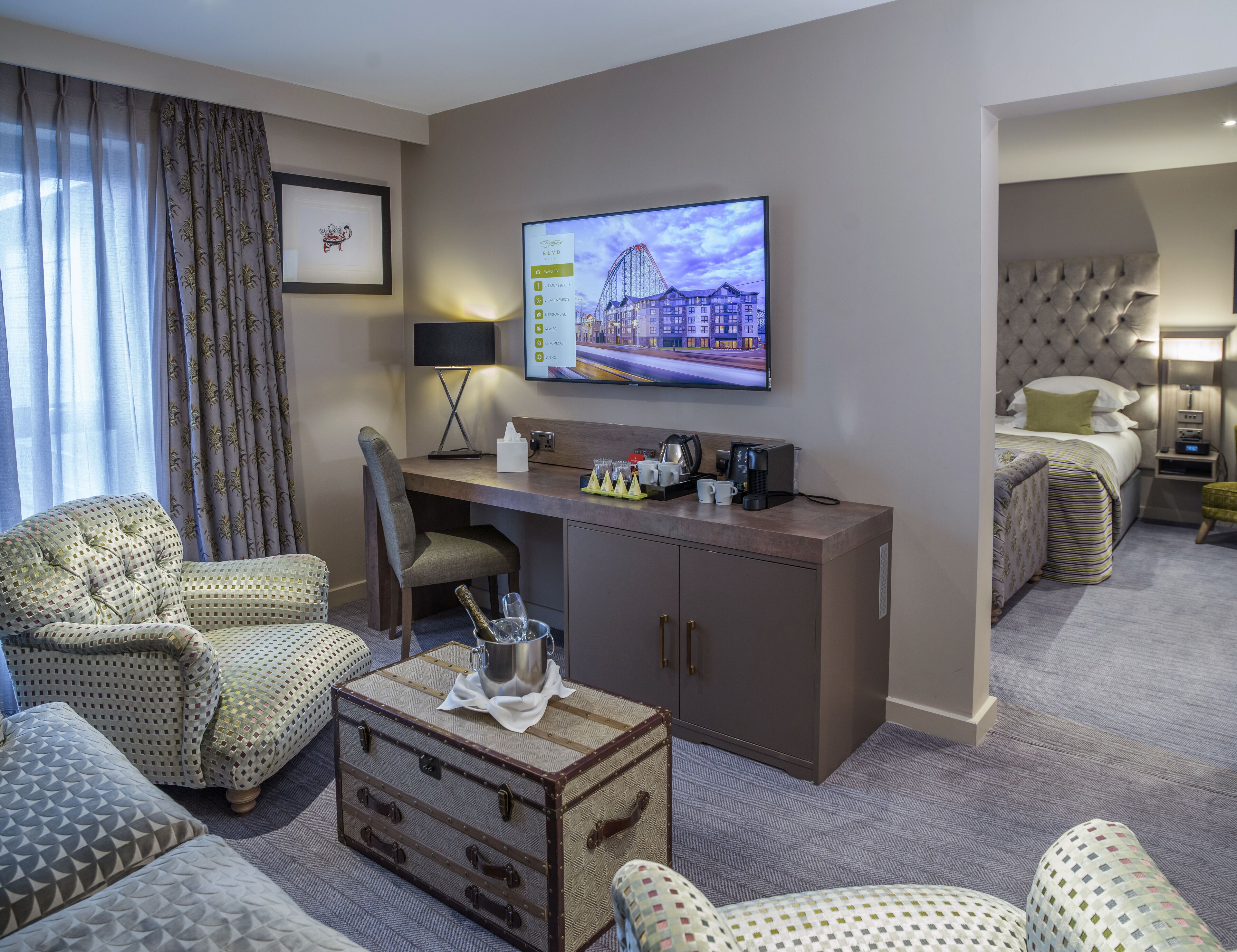 Una habitación de hotel con escritorio, sillas, televisor, cama y minibar.