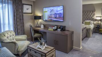 Una habitación de hotel con escritorio, sillas, televisor, cama y minibar.