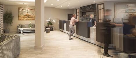A modern hotel lobby with a reception desk, seating area, and decorative plants.