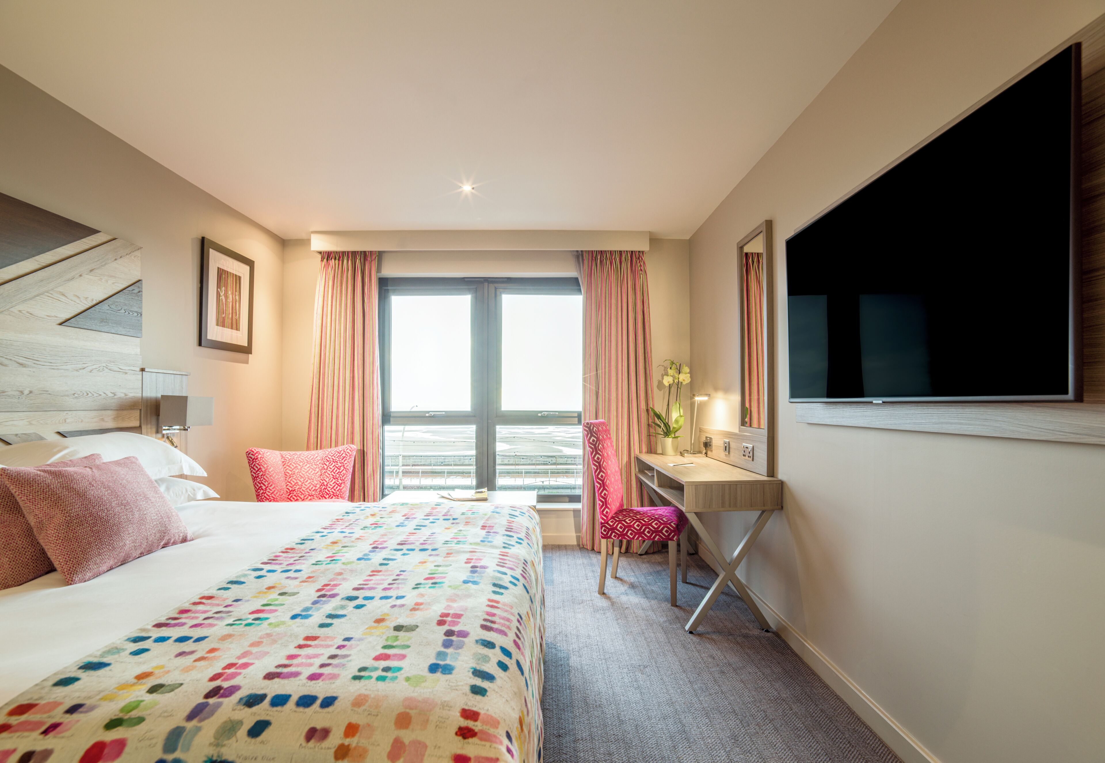 A hotel room with a bed, desk, chair, and a large window with curtains.