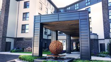 Een modern gebouw met een overdekte entree, een bolvormig sculptuur en een aangelegde tuin.