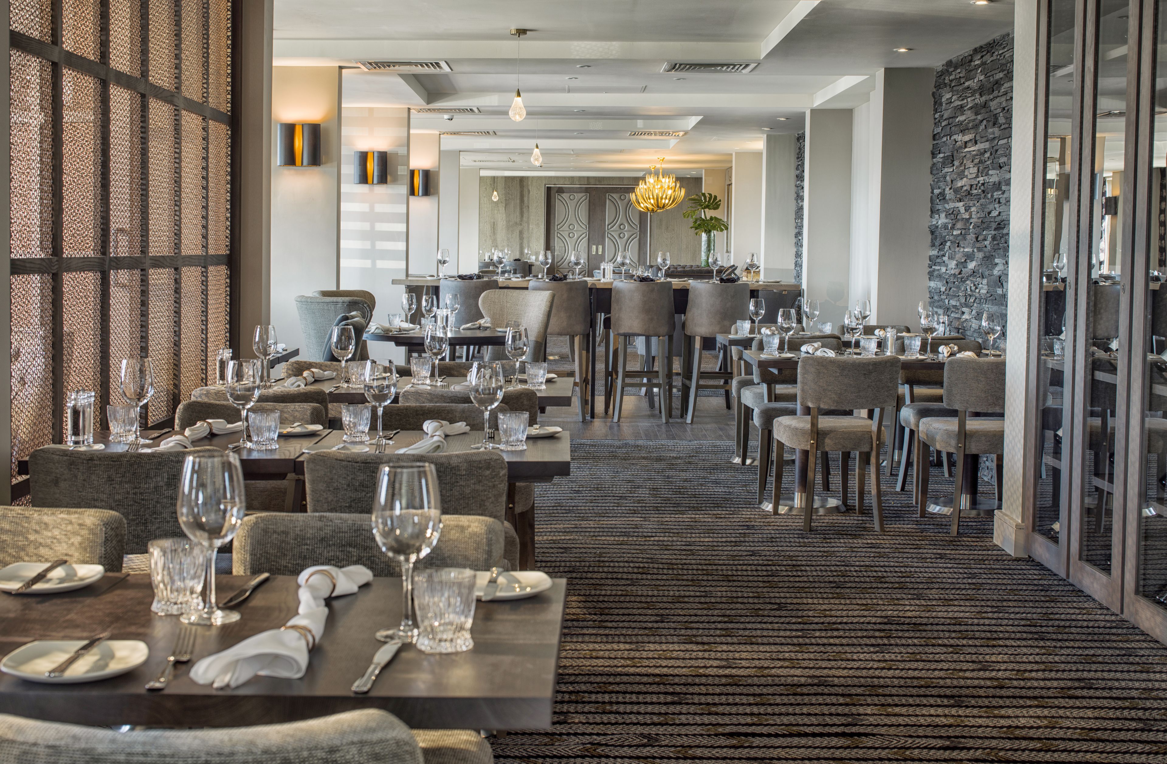 A spacious hotel dining area with multiple tables set for guests, featuring a modern design with neutral tones and a patterned carpet.