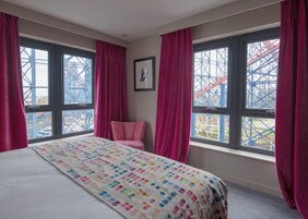 Hotellihuone, jossa on sänky, tuoli ja suuret ikkunat, joissa on verhot.