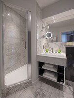 Een moderne badkamer met een douchecabine van glas, een marmeren vloer en een wastafel met een spiegel en twee groene glazen flessen.