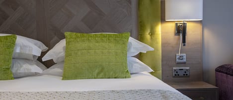 A neatly made bed with green and white pillows, a wooden headboard, and a bedside table with a lamp.