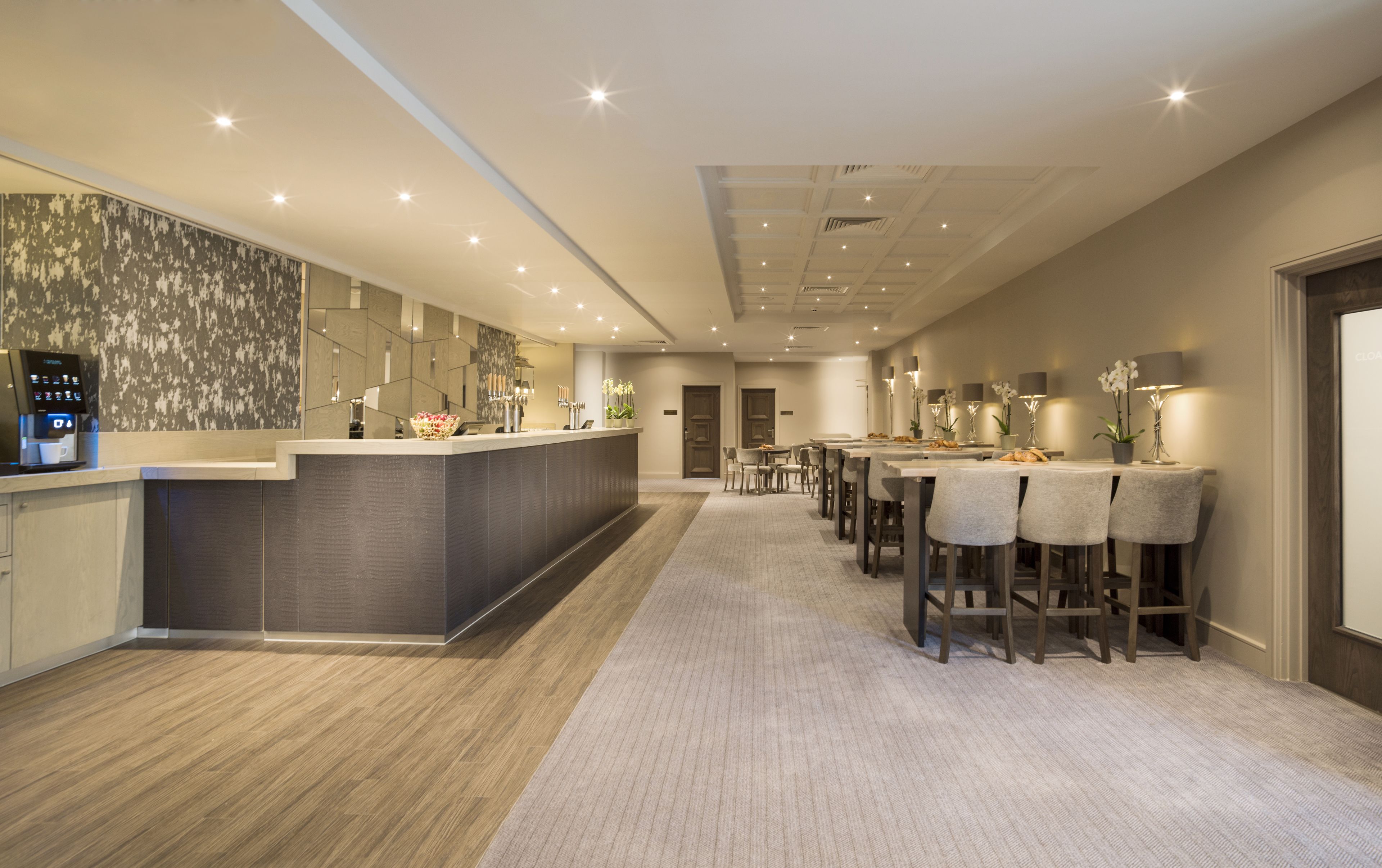 A modern hotel lobby with a reception desk, a bar area, and a dining space with chairs and tables.