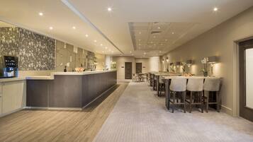 Un moderno hall de hotel con mostrador de recepción, área de bar y comedor con sillas y mesas.