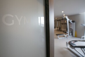 Een onscherp zicht op de binnenkant van een sportschool, met fitnessapparatuur en een deur waarop 'GYM' staat.