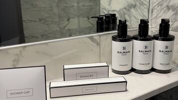 A bathroom vanity with a marble countertop, a mirror, and various toiletries including a shaving kit, dental kit, and Balmain Paris body wash.