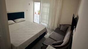 Un dormitorio con cama, sofá y una mesita. Hay una ventana con cortinas y vistas al exterior.