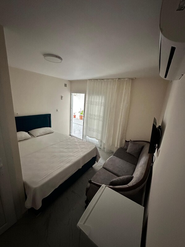 Un dormitorio con cama, sofá y una mesita. Hay una ventana con cortinas y vistas al exterior.