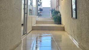 Un pasillo con suelo de baldosas, cuadros en las paredes y vistas al exterior a través de puertas de cristal.