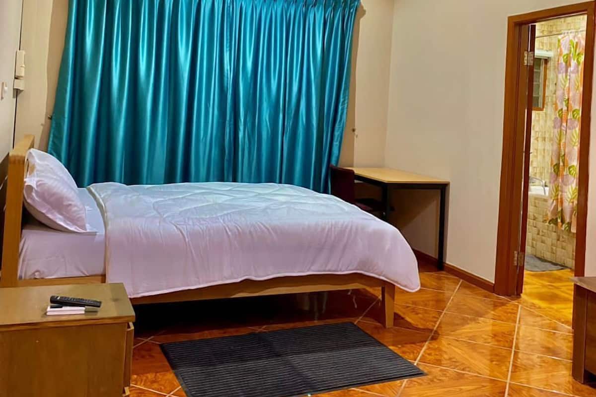 A bedroom with a bed, a nightstand, a desk, a ceiling fan, and an air conditioning unit.