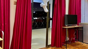 A room with red curtains, a television on a stand, and a patterned floor. - GHouse Accra (Adenta)