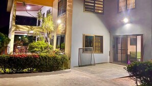 A two-story building with a covered patio area, large windows, and a gated entrance. - GHouse Accra (Adenta)