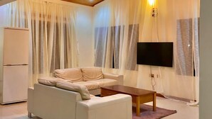 A modern living room with a sofa, a coffee table, a flat-screen TV, and a ceiling fan. - GHouse Accra (Adenta)