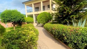 A two-story building with a balcony, surrounded by well-maintained hedges and a clear sky. - GHouse Accra (Adenta)