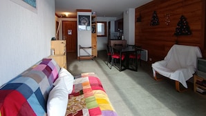 Un salon chaleureux avec un canapé coloré, une table à manger avec des chaises, un fauteuil blanc et un petit meuble pour la télévision.