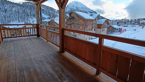 Un balcon en bois offrant une vue sur des bâtiments et des montagnes enneigés.