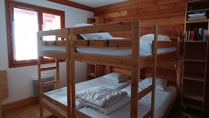 Une chambre avec un lit superposé, des murs en bois, une fenêtre et une bibliothèque.