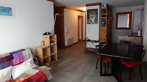 Un salon comprenant un canapé, une table à manger avec des chaises, une bibliothèque et un téléviseur.