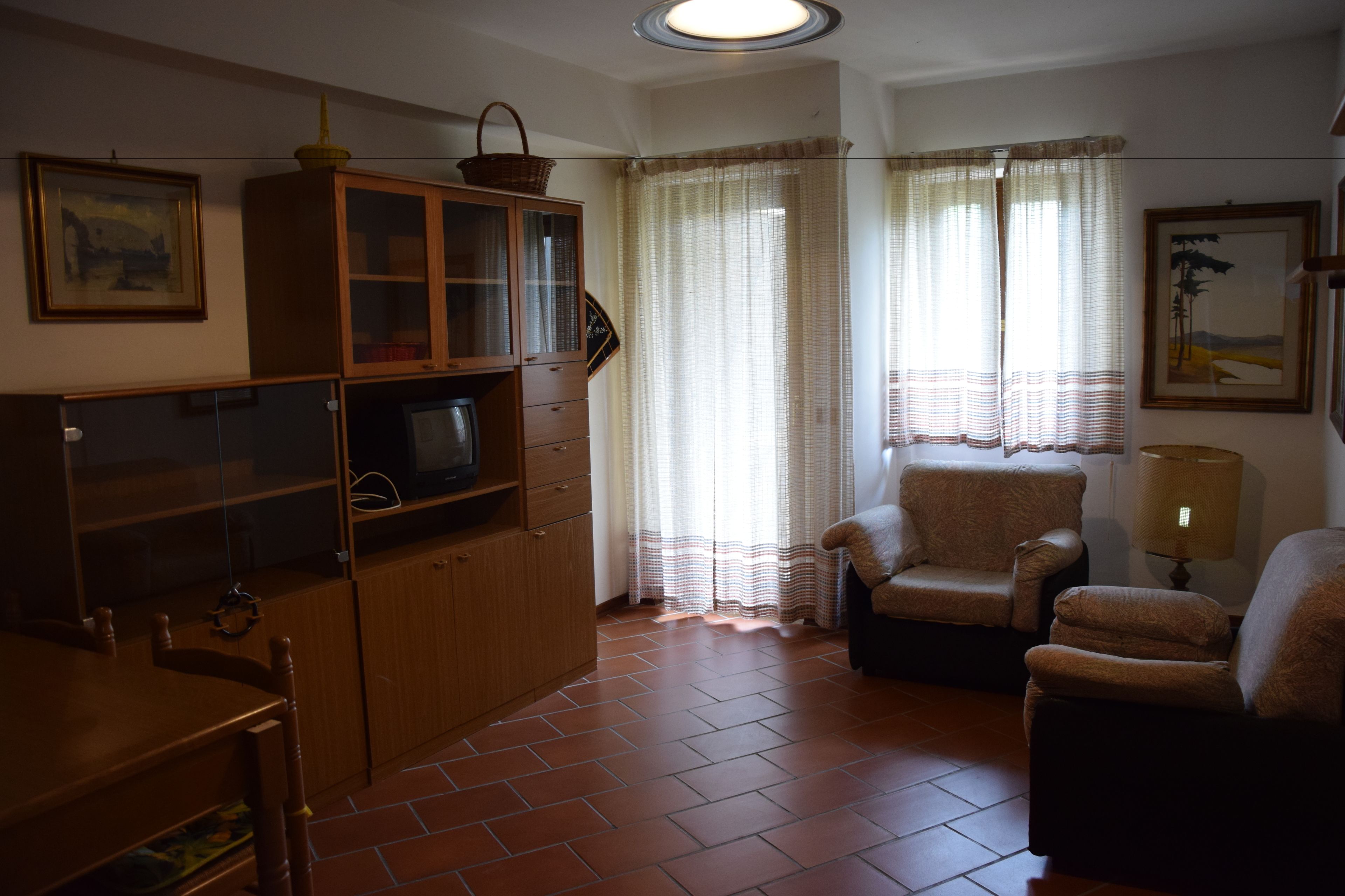 Un soggiorno con televisore, mobiletti in legno, un divano e una lampada.