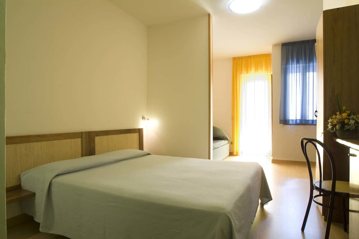 A room with a bed, a desk, and a chair. There is a window with curtains.