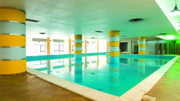 An indoor swimming pool with tiled flooring and pillars with yellow and white stripes. - Magara Hotel (Spezzano della Sila)