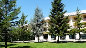 A courtyard with a lawn, several trees, and a building with multiple balconies and windows. - Magara Hotel (Spezzano della Sila)