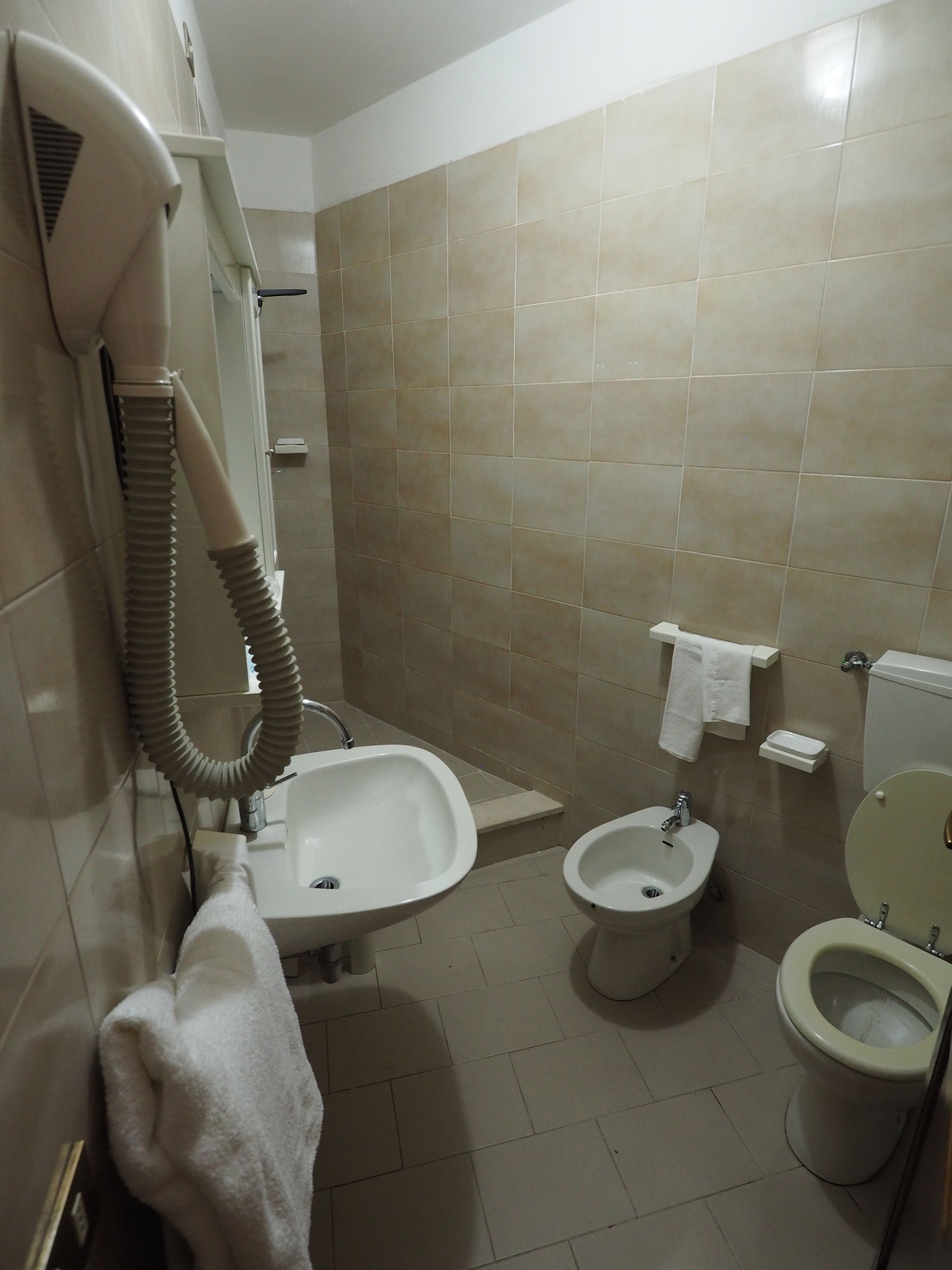 Un bagno con lavandino, bidet, toilette e asciugacapelli montato a parete.