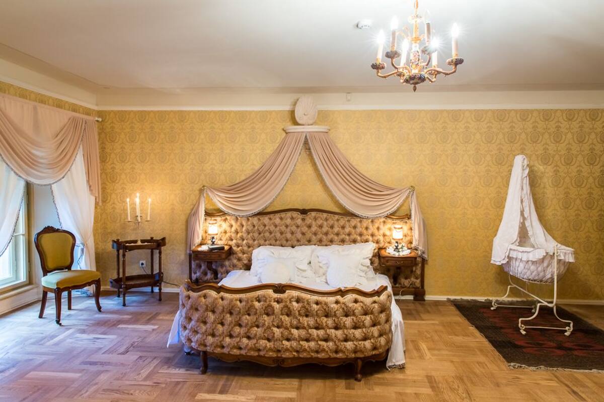 A bedroom with a large bed, a chandelier, a chair, and a nightstand with candles.