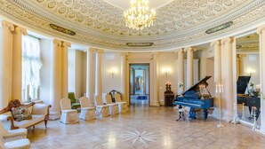 Un salón majestuoso con un piano, columnas ornamentadas y una araña.