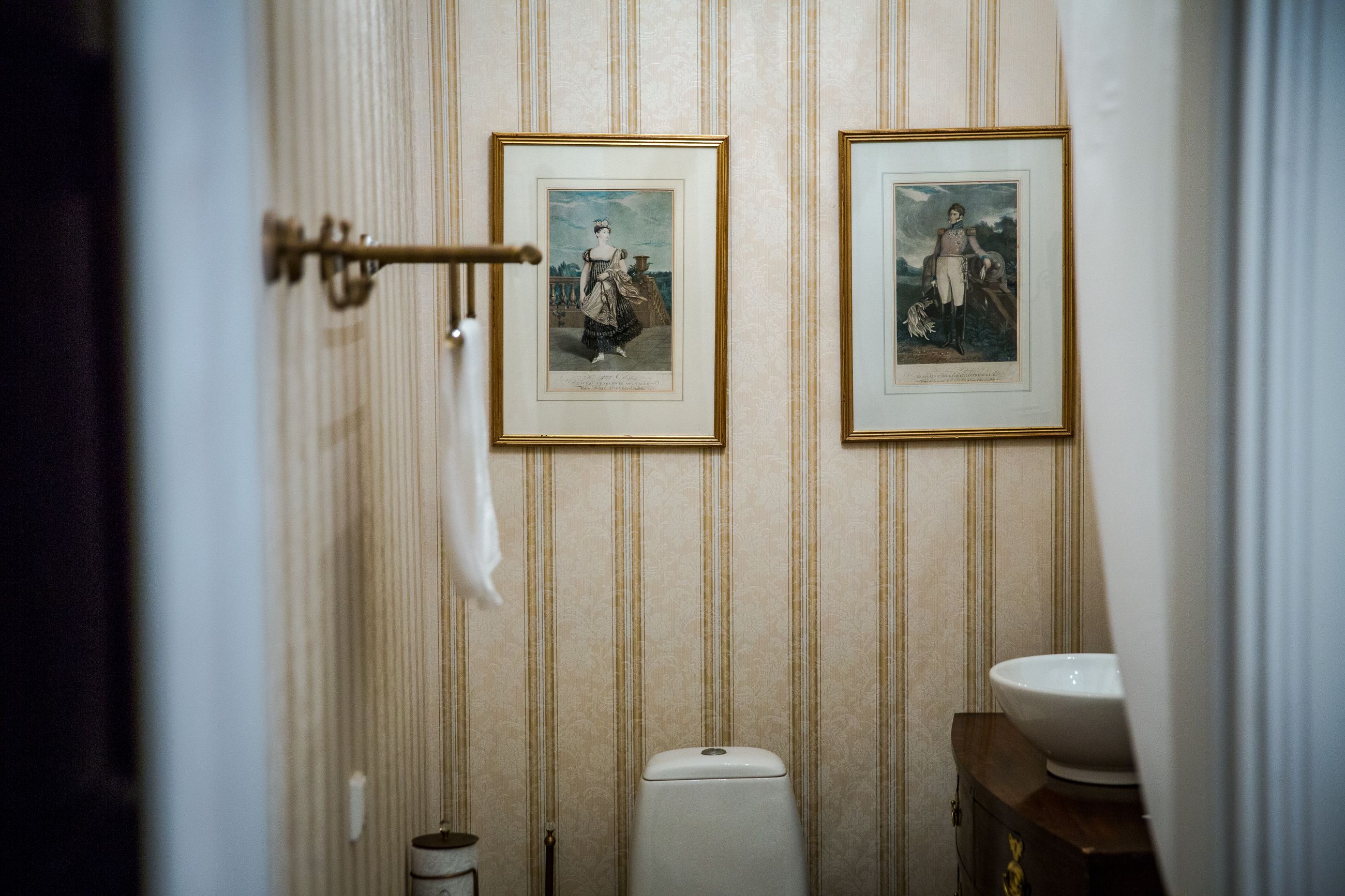 Un baño con papel tapiz a rayas, un inodoro y dos cuadros en la pared.