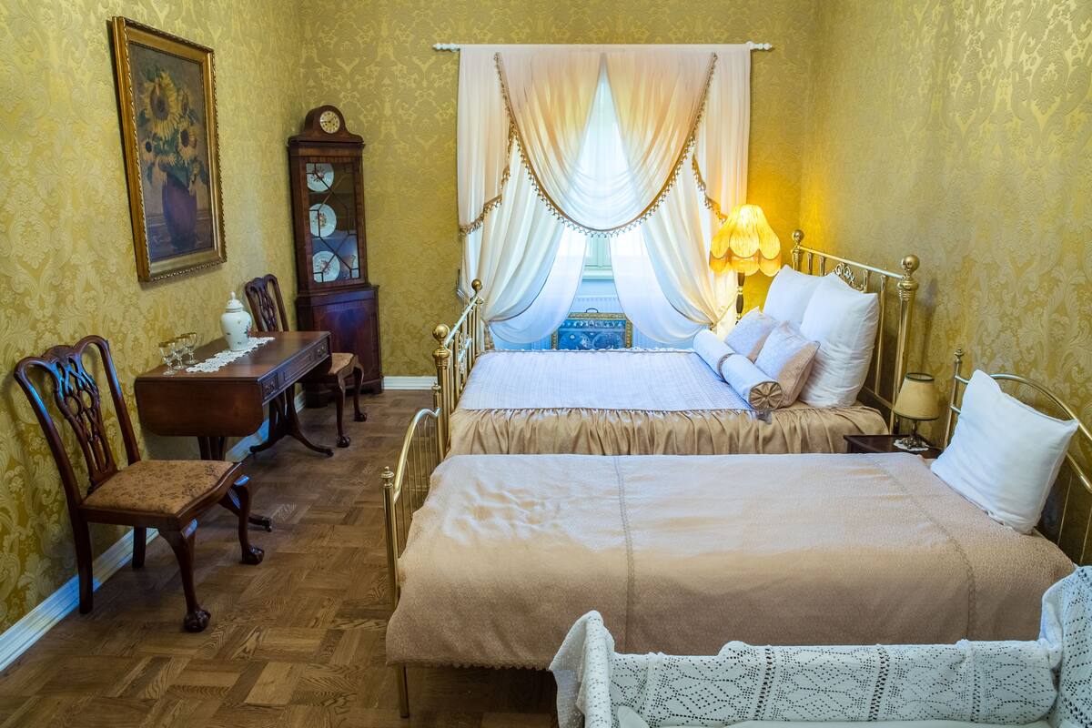 A bedroom with a large bed, a desk with chairs, a clock, and a window with curtains.