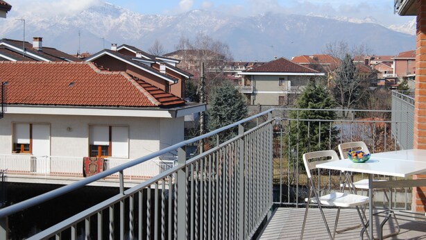 A balcony with a table and chairs, overlooking a residential area with houses and a mountain range in the background. - B&B Le Terrazze Boutique Hotel 2 Torino (Cirie)