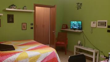 Un dormitorio con una cama, una silla, un escritorio, un televisor y un armario.