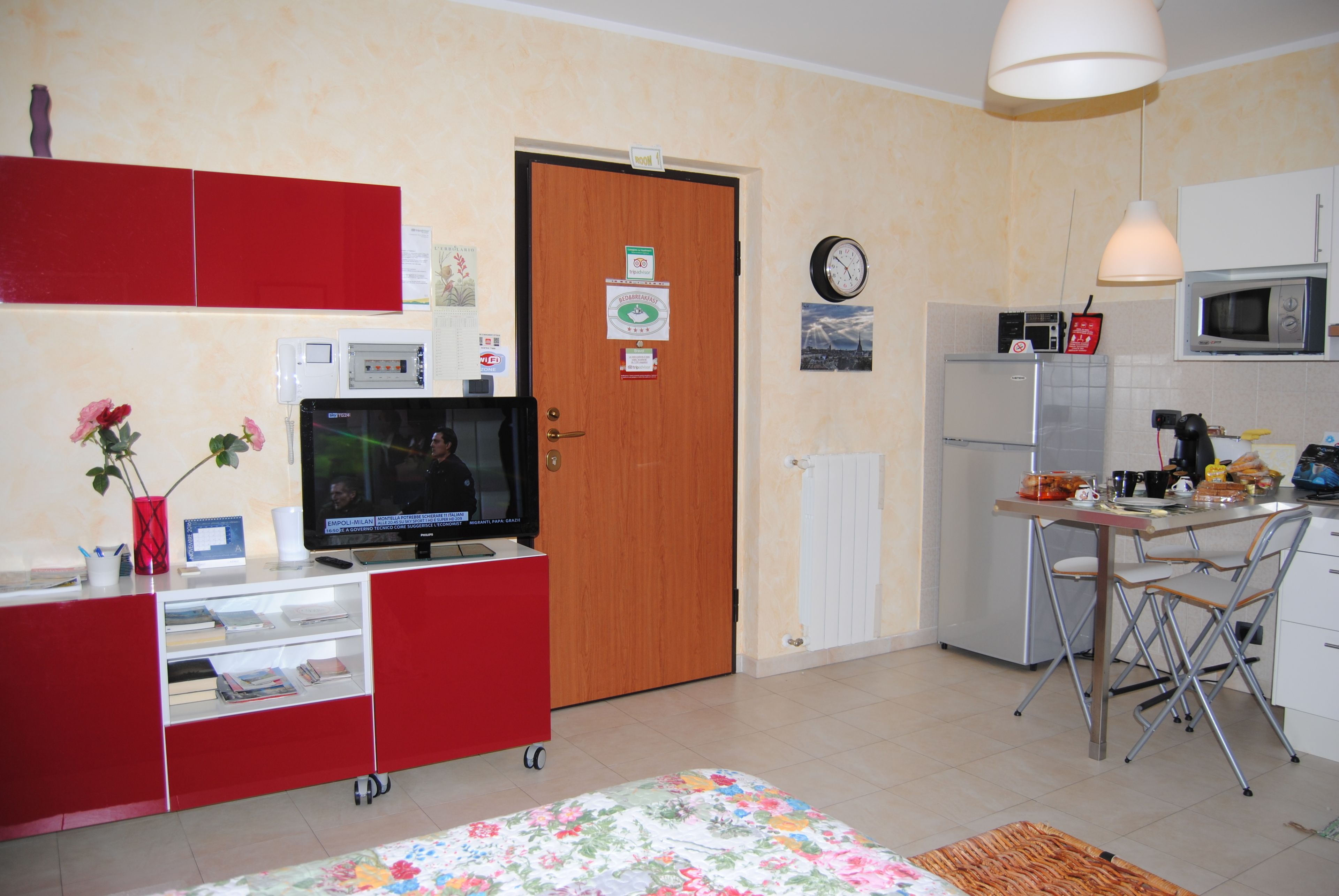 A compact living space with a kitchenette, a television, a red cabinet, and a wooden door.