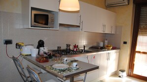 A compact kitchen with a microwave, stove, and sink. There are chairs and a table with a placemat. - B&B Le Terrazze Boutique Hotel 2 Torino (Cirie)