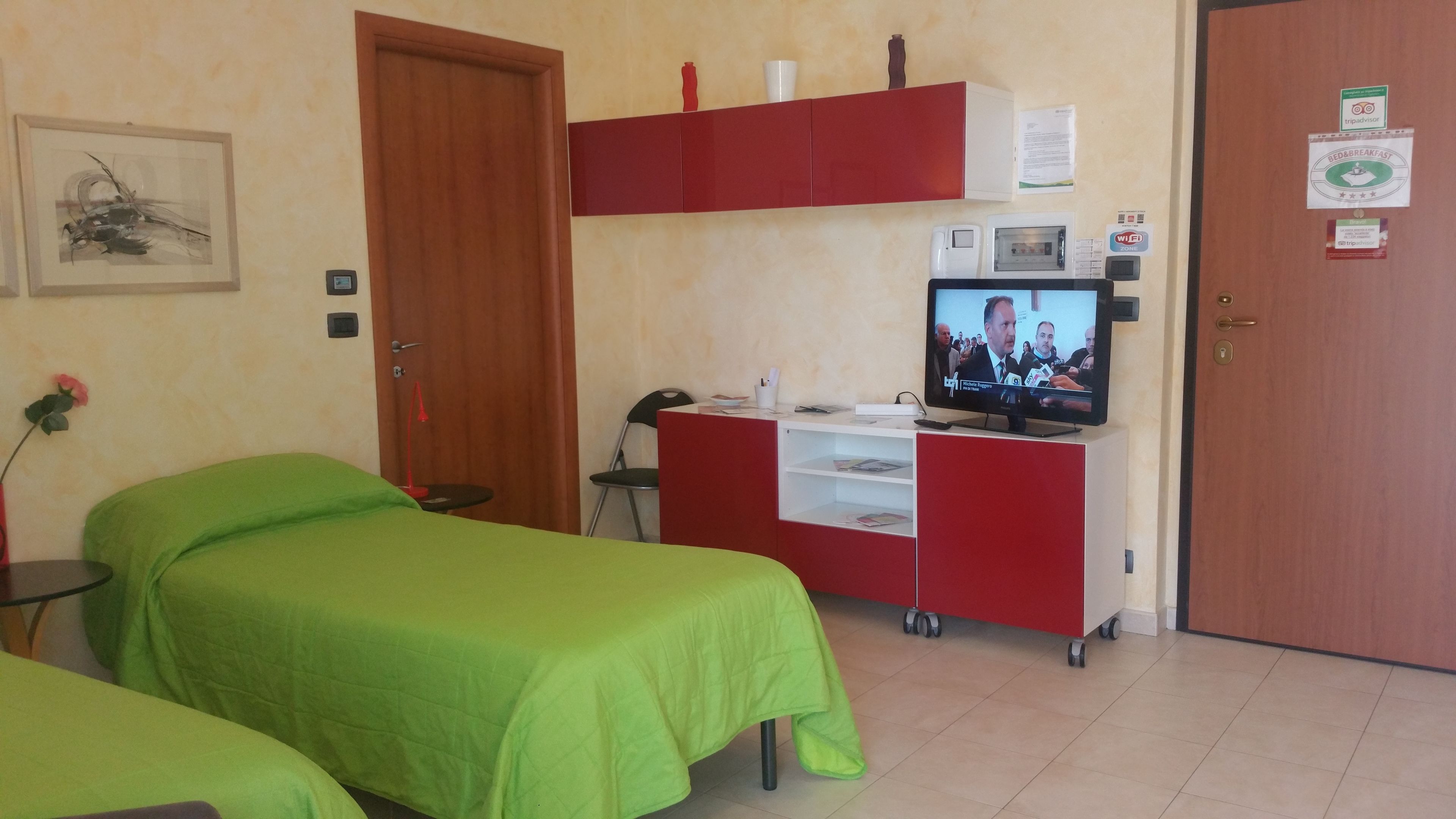 Une chambre d’hôtel avec deux lits simples, un bureau avec une télévision, un minibar et une porte portant une pancarte indiquant « zone Wi-Fi ».