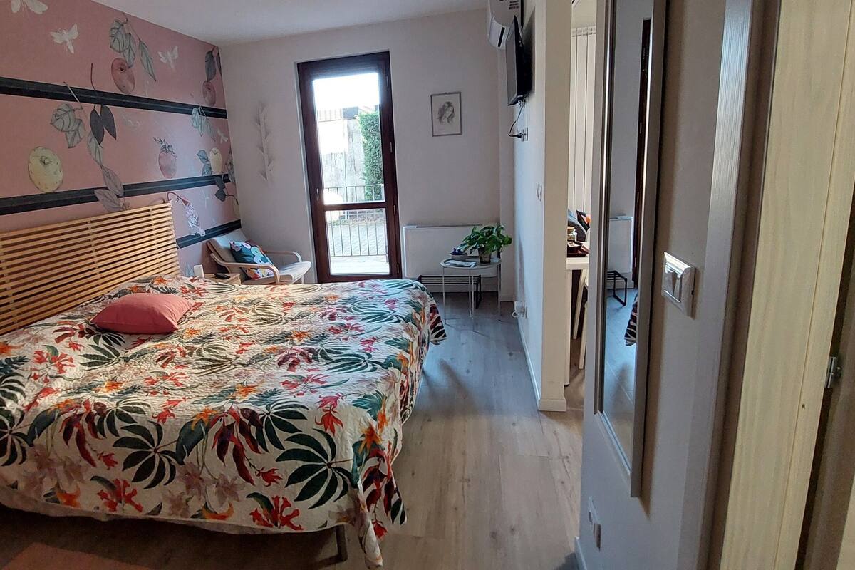 Un dormitorio con una cama, una silla, una mesita con una planta y una ventana.