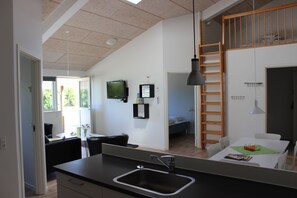 A modern kitchen with a large island, a dining area with a table and chairs, a loft bedroom with a ladder, and a TV mounted on the wall. - Fitting Landsbyferie Apartments (Vorbasse)