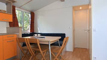 Een kleine keuken met een eettafel en stoelen, een raam met gordijnen, en een deur.