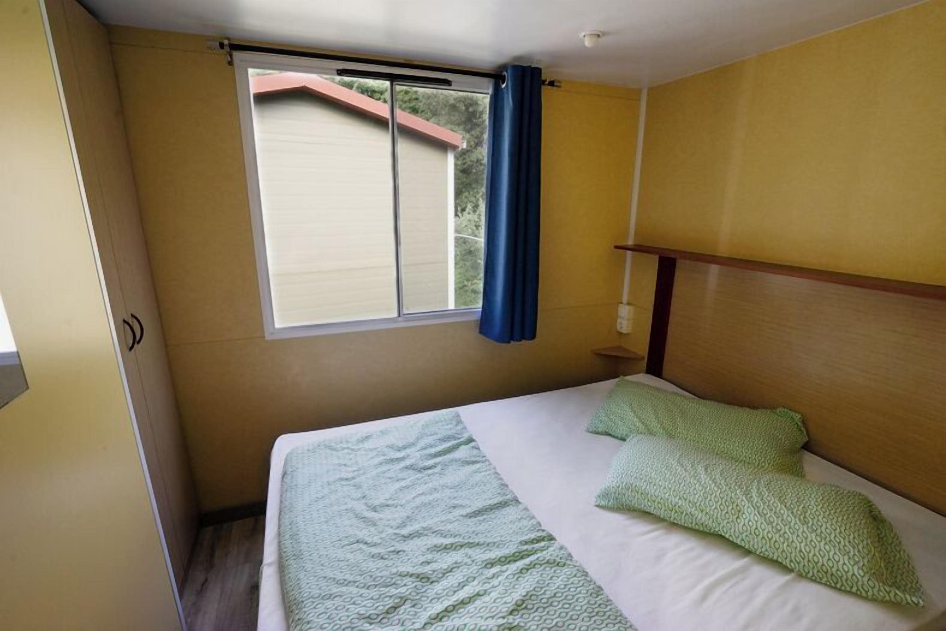 A small, single-bed room with a window, a curtain, and a wooden headboard.
