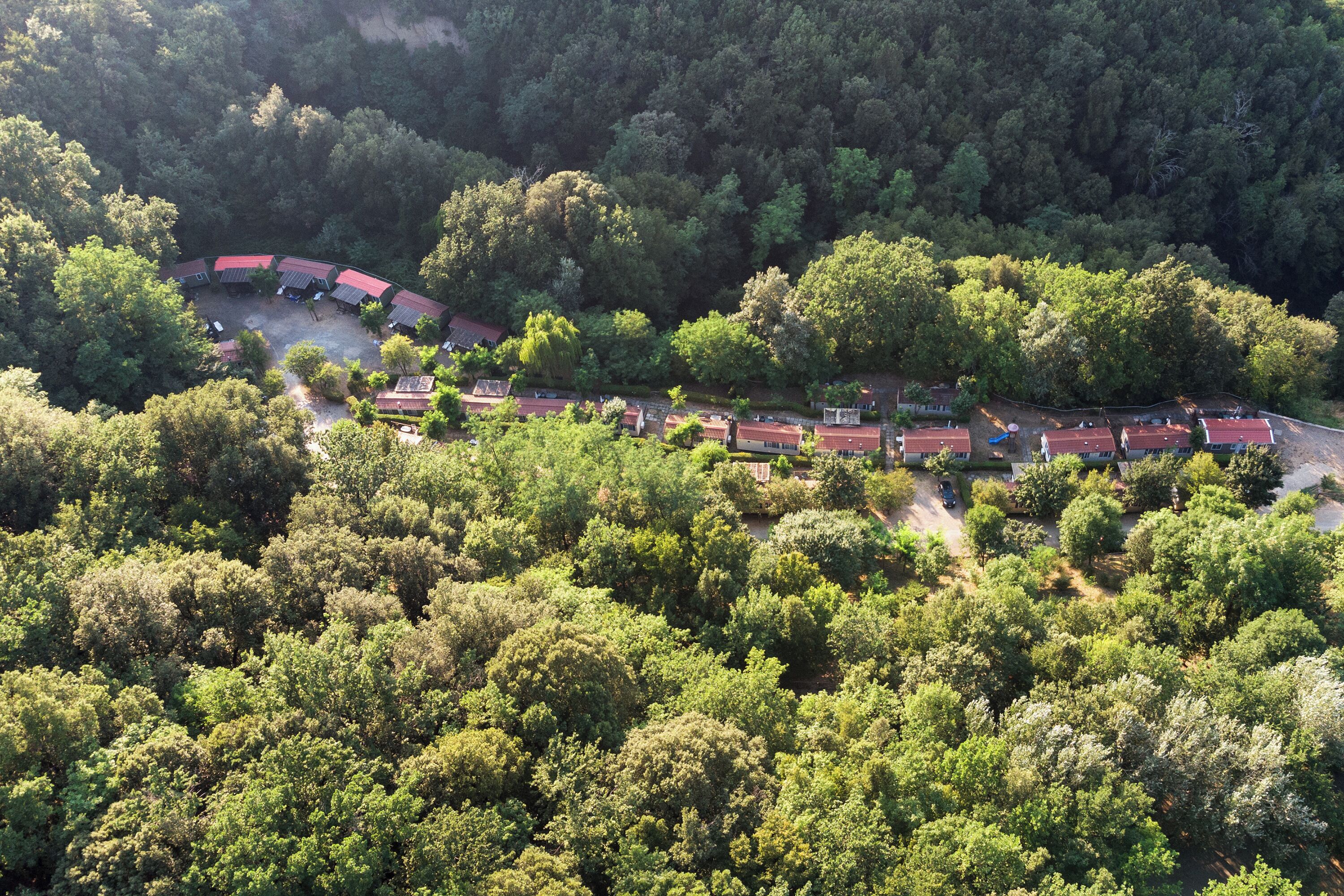 An aerial view of a resort with a curved layout of buildings surrounded by dense forest.