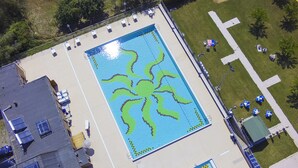 Vista aérea de una piscina con un diseño de mosaico único, rodeada de sillas de descanso y sombrillas.