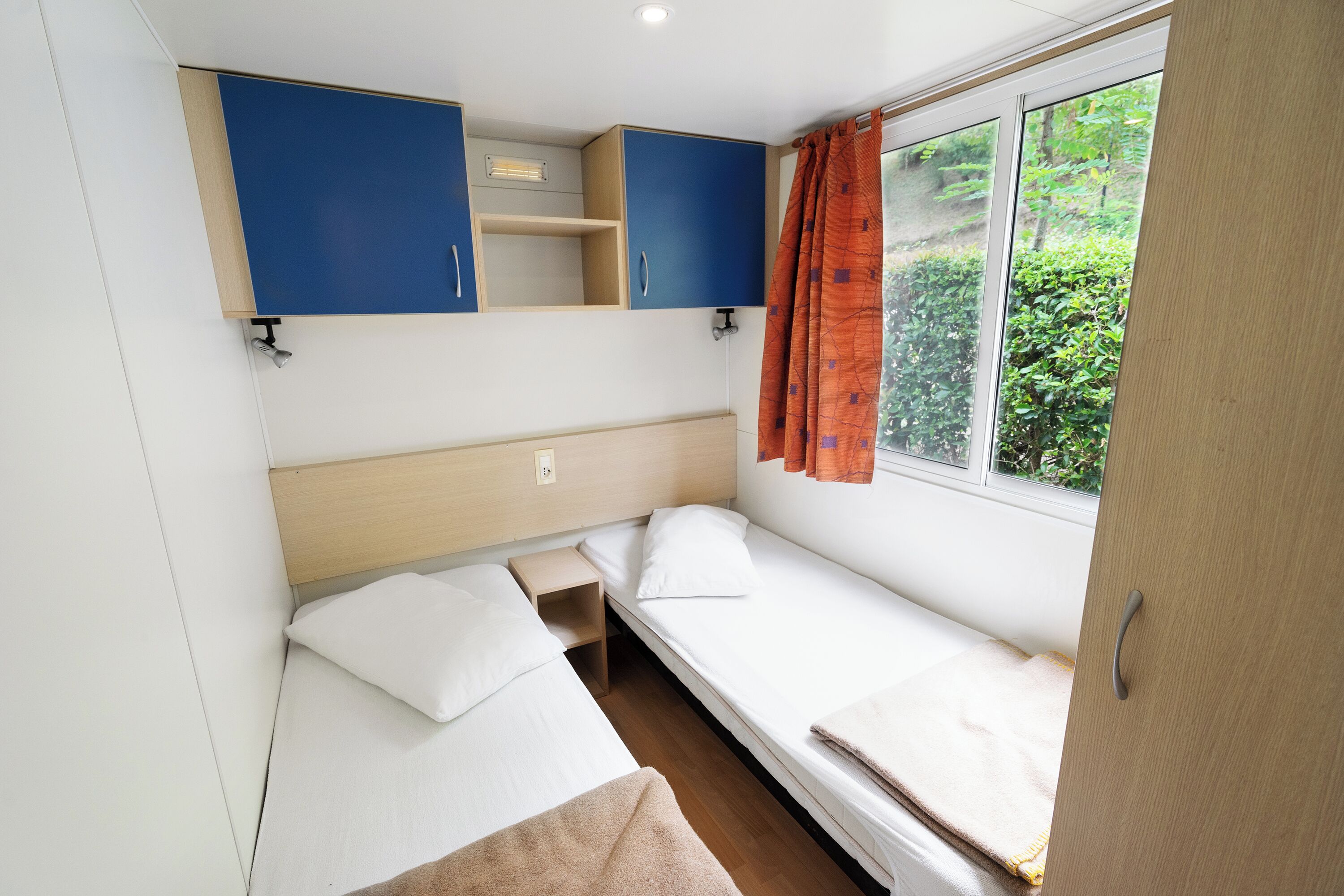 Une petite chambre avec un lit simple, une tête de lit en bois, une petite table de chevet et une fenêtre avec des rideaux.
