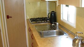 A compact kitchen with a gas stove, a sink, and a kettle.