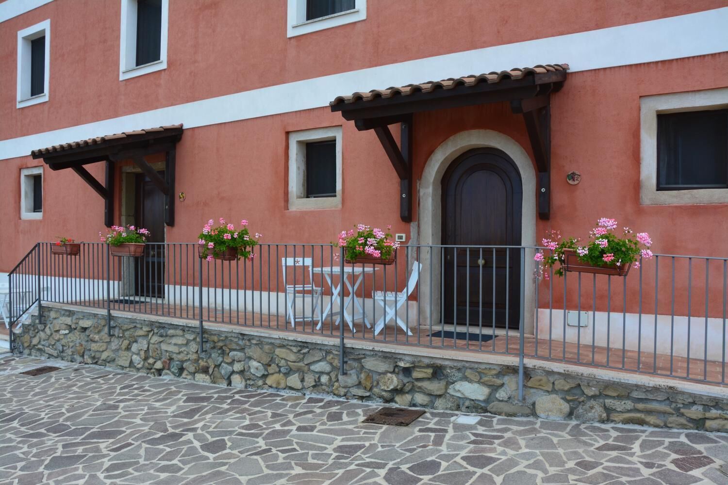 A building with a stone facade, a tiled roof, and a balcony with a table and chairs.